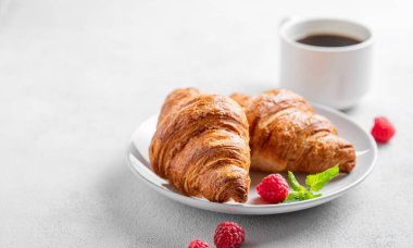 Bir fincan espresso kahve ve taze ahududu ile kruvasan ve sabah ışıklarıyla beyaz desenli bir tabakta nane şekeri. Sağlıklı yemek ve Fransız kahvaltısı kavramı. Boşluğu kopyala.