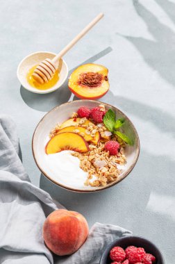 Doğal yoğurt, yulaf gevreği, müsli, şeftali, ahududu ve bal, taze meyve, böğürtlen ve sabah gölgesiyle mavi bir arka planda. Sağlıklı ve besleyici kahvaltı konsepti