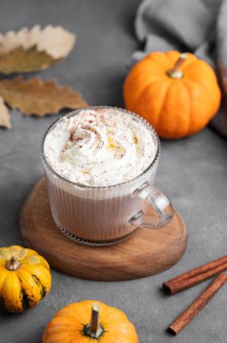 Süslü balkabağı ve tarçın çubuğuyla ahşap zemin üzerinde cam bardakta kremalı baharatlı latte. Moda sonbahar ılık içeceği kavramı. Üst görünüm.