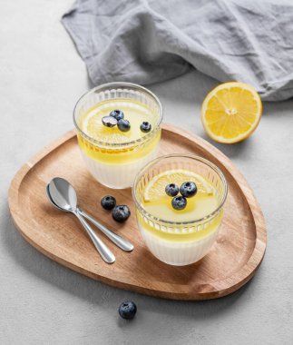 Böğürtlenli, peçeteli ve kaşıklı iki bardakta yaban mersinli limon panna cotta. Geleneksel İtalyan tatlı konsepti. 