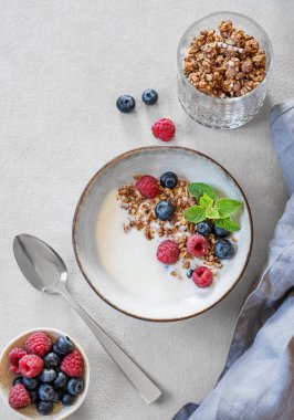 Yunan yoğurdu, ahududu ve böğürtlenlerle bembeyaz arka planda taze böğürtlen ve kaşıkla bembeyaz bir kasede düz bir mısır gevreği. Süt ürünlerinin kahvaltısı, sabah ışığında yulaf ezmesi. Üst görünüm.