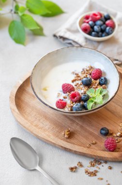Yunan yoğurdu, ahududu ve böğürtlenli granola beyaz arka planda, ahşap bir tahtanın üzerinde taze böğürtlenli yaban mersini. Süt ürünlerinin kahvaltısı, sabah ışığında yulaf ezmesi.. 