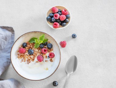 Yunan yoğurdu, ahududu ve böğürtlenli granola beyaz arka planda taze böğürtlen ve kaşıkla bir kasede. Süt ürünlerinin kahvaltısı, sabah ışığında yulaf ezmesi. Üst görünüm 