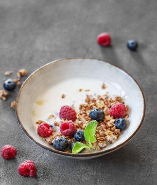Yunan yoğurdu, ahududu ve böğürtlenli granola koyu arkaplanda, taze böğürtlenli. Süt ürünleri ve yulaf ezmesinden yapılmış ev yapımı kahvaltı konsepti. Boşluğu kopyala.