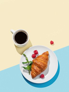 Beyaz tabakta taze kruvasan, ahududu ve sarı ve mavi arka planda bir fincan espresso kahvesi. Kahvaltı pastası modeli ya da afiş için tasarım konsepti. Üst görünüm ve kopyalama alanı.