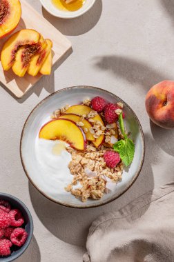Yunan yoğurdu yulaf ezmesi veya müsli, şeftali ve ahududu arkaplanda taze meyve, böğürtlen ve sabah gölgesi olan bir kasede. Sağlıklı ve besleyici kahvaltı konsepti. Üst görünüm.