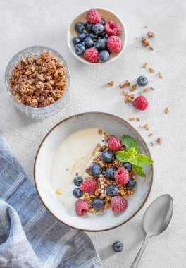 Yunan yoğurdu, ahududu ve böğürtlenlerle bembeyaz arka planda taze böğürtlen ve kaşıkla bembeyaz bir kasede düz bir mısır gevreği. Süt ürünlerinin kahvaltısı, sabah ışığında yulaf ezmesi.. 