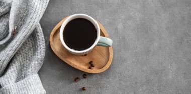 Kahve çekirdekleri ve rahat gri bir süveteri olan koyu renkli bir arka planda, tahta bir tahtanın üzerindeki fincanda Espresso kahvesi. Sonbahar havasında sabah içkisi kavramı. Üst görünüm ve kopyalama alanı.