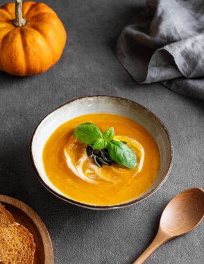 Kremalı, fesleğenli ve tohumlu ev yapımı balkabağı çorbası. Ekmek, kaşık ve peçeteyle birlikte. Kırsal tarzda sağlıklı ve rahat sonbahar yemekleri kavramı. 