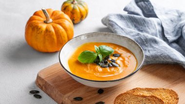 Kremalı, fesleğenli ve tohumlu ev yapımı balkabağı çorbası ahşap bir tahtada ekmek ve peçeteyle birlikte taze balkabaklarıyla birlikte. Sağlıklı ve samimi sonbahar yemekleri kavramı. Boşluğu kopyala.