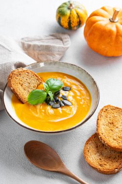 Kremalı balkabağı çorbası, fesleğen ve tohumlar. Ekmek, kaşık ve taze balkabaklarıyla birlikte. Sağlıklı, rahat ve rahat sonbahar yemekleri kavramı. 