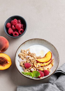 Yunan yoğurdu yulaf ezmesi veya müsli, şeftali ve ahududu arkaplanda taze meyve, dut ve peçeteyle birlikte. Sağlıklı ve besleyici kahvaltı konsepti. Üst görünüm ve kopyalama alanı.