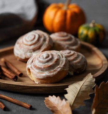 Tarçınlı çörekler ve balkabaklı, karanlık bir arka planda, ahşap bir tahta üzerindeki krema. Kahvaltıda geleneksel İsveç çöreklerini kırsal tarzda kavra. Sıcak sonbahar ev yapımı pişirme.