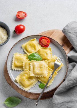 Ev yapımı ravioli makarna peynirli, domatesli ve fesleğenli tahta bir tabakta peçete ve çatallı. Geleneksel İtalyan yemeği konsepti. Üst görünüm ve kopyalama alanı.