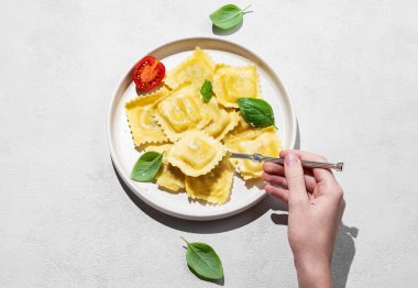 Parmesanlı ev yapımı ravioli makarna, domates ve gölgeli fesleğen ile el ele tutuşan çatal. Geleneksel İtalyan yemeği konsepti. Üst görünüm ve kopyalama alanı.