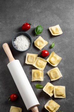 Düz makarna, domates ve fesleğenli ravioli, koyu arkaplan, un ve oklavalı. Geleneksel İtalyan yemeği konsepti. Üst görünüm ve kopyalama alanı.