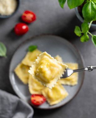 Ev yapımı ravioli makarna, peynirli, domatesli ve fesleğenli peçete ve çatallı koyu bir arka planda. Geleneksel İtalyan yemeği konsepti. Üst görünüm.
