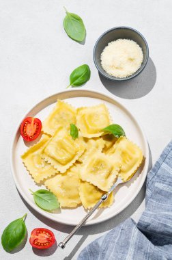 Parmesanlı Ravioli makarnası, domates ve fesleğen, arka planda gölgeli ve peynirli bir tabakta. Geleneksel İtalyan ev yapımı yemek konsepti. Üst görünüm ve kopyalama alanı.