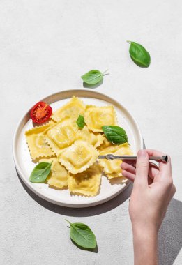Parmesanlı ev yapımı ravioli makarna, domates ve gölgeli fesleğen ile el ele tutuşan çatal. Geleneksel İtalyan yemeği konsepti. Üst görünüm ve kopyalama alanı.