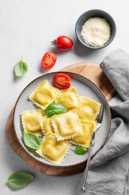 Ev yapımı ravioli makarna peynirli, domatesli ve fesleğenli tahta bir tabakta peçete ve çatallı. Geleneksel İtalyan yemeği konsepti. Üst görünüm ve kopyalama alanı.