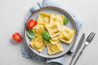 Ev yapımı ravioli makarna peynirli, domatesli, fesleğenli ve peçeteli bir tabakta çatallı. Geleneksel İtalyan yemeği konsepti. Üst görünüm ve kopyalama alanı.