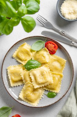 Peynirli, domatesli ve fesleğenli ev yapımı ravioli makarnası. Çatal, bitki ve peçeteyle hafif bir arka planda. Geleneksel İtalyan yemeği konsepti. Üst görünüm.