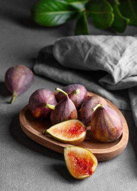 Yapraklar ve peçeteyle birlikte siyah arka planda, ahşap bir tabakta sulu incir. Kırsal tarzda sağlıklı ve lezzetli meyveler kavramı.