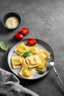 Ev yapımı ravioli makarna, peynirli, domatesli ve fesleğenli peçete ve çatallı koyu bir arka planda. Geleneksel İtalyan yemeği konsepti. Üst görünüm ve kopyalama alanı.