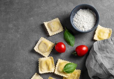 Düz makarna, domates ve fesleğenli ravioli, koyu arka planda un ve peçeteyle. Geleneksel İtalyan yemeği konsepti. Üst görünüm ve kopyalama alanı.