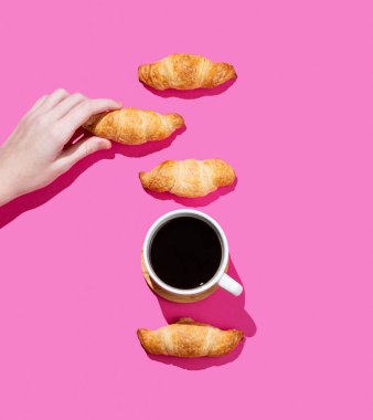 Elinde taze kruvasan ya da pembe arka planda bir fincan espresso kahveli simit var. Kahvaltı pastası modeli ya da afiş için tasarım konsepti. Üst görünüm ve kopyalama alanı.