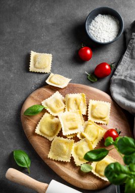 Düz makarna ravioli, domates ve fesleğen ile kaplanmış koyu arkaplan üzerinde un, peçete ve oklavayla. Geleneksel İtalyan yemeği konsepti. Üst görünüm ve kopyalama alanı.