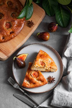 İncirli turta. Koyu arka planda bir tabakta taze meyve ve yapraklı lezzetli bir sünger keki. Ev yapımı pişirme konsepti. Üst görünüm.