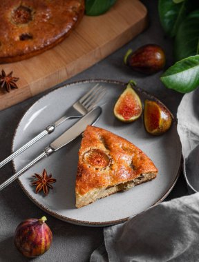 İncirli turta. Koyu arka planda bir tabakta taze meyve ve yapraklı lezzetli bir sünger keki. Ev yapımı pişirme konsepti. 