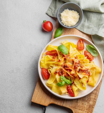 Domates soslu Tagliatelle makarnası, fesleğen ve parmesan peyniri açık arkaplanda tahta bir tabakta. Geleneksel ev yapımı İtalyan yemeği kavramı. Üst görünüm ve kopyalama alanı.