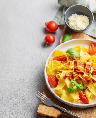 Domates soslu Tagliatelle makarnası, fesleğen ve parmesan peyniri açık arkaplanda tahta bir tabakta. Geleneksel ev yapımı İtalyan yemeği kavramı. Üst görünüm ve kopyalama alanı.