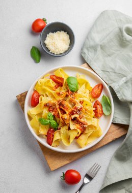 Domates soslu, fesleğenli ve parmesan peynirli tagliatelle makarnası, tahta bir tabakta, açık arkaplanda. Geleneksel ev yapımı İtalyan yemeği kavramı. Üst görünüm ve kopyalama alanı.