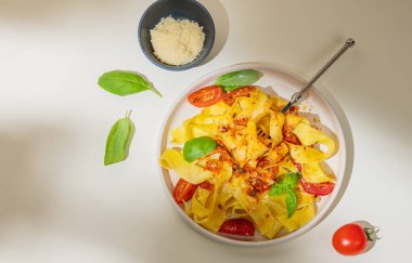 Tagliatelle ya da domates soslu pappardelle makarna, fesleğen ve parmesan peyniri, çatallı ve gölgeli sarı bir tabakta. Modern bir İtalyan yemeği tasarımı ya da reklamı konsepti.
