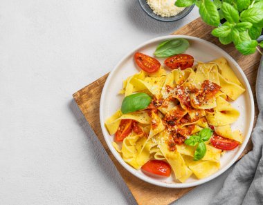 Domates soslu, fesleğenli ve parmesan peynirli ev yapımı tagliatelle makarnası, tahta bir tabakta, arka planda hafif bir arka planda. Geleneksel İtalyan yemeği kavramı. Üst görünüm ve kopyalama alanı.
