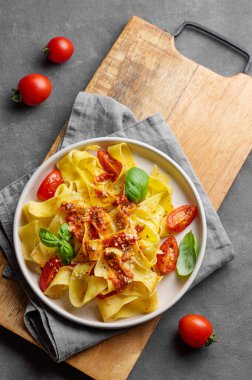 Tagliatelle makarnası, domates sosu, fesleğen ve parmesan peyniri. Tahta bir tabakta, karanlık bir arka planda. Geleneksel ev yapımı İtalyan yemeği kavramı. Üst görünüm ve kopyalama alanı.