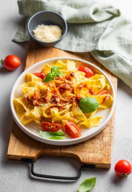 Domates soslu Tagliatelle makarnası, fesleğen ve parmesan peyniri tahta bir tabakta, arka planda hafif bir peçeteyle. Geleneksel ev yapımı İtalyan yemeği kavramı.. 