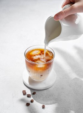 Kahve çekirdekleri ve gölgeli hafif bir arka planda süt sürahisinden el yapımı soğuk sütlü kahve bardağı. Yaz ferahlatıcı moda içecek konsepti. Boşluğu kopyala.