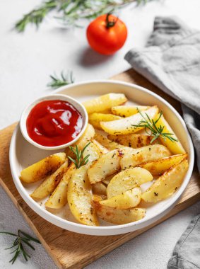 Baharatlı fırında patates, taze biberiye ve ahşap bir tahta üzerinde domates sosu. Ev yapımı vejetaryen atıştırmalık konsepti.