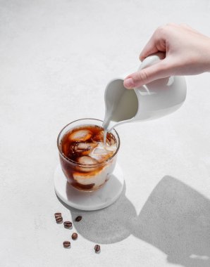 Kahve çekirdekleri ve gölgeli hafif bir arka planda süt sürahisinden el yapımı soğuk sütlü kahve bardağı. Yaz ferahlatıcı moda içecek konsepti. Üst görünüm ve kopyalama alanı.