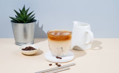 Kahve çekirdekleri, ev bitkisi, süt sürahisi ve gölgeli sarı ve mavi arka planda sütlü soğuk latte kahve. Yaz modası ferahlatıcı içecek konsepti. Ön görünüm.