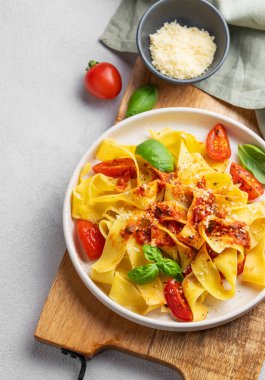 Domates soslu Tagliatelle makarnası, fesleğen ve parmesan peyniri açık arkaplanda tahta bir tabakta. Geleneksel ev yapımı İtalyan yemeği kavramı. Üst görünüm ve kopyalama alanı.