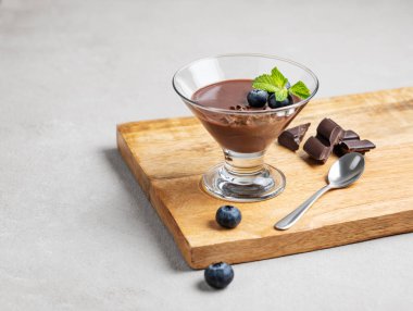 Taze yaban mersinli bardakta çikolatalı puding ve arka planda böğürtlenli ve kaşıklı bir tahta üzerinde nane şekeri. Ev yapımı kremalı tatlı ya da panna cotta konsepti. Boşluğu kopyala.