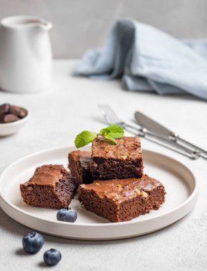 Fındıklı çikolatalı browni. Yaban mersinli bir tabakta parçalara kesilmiş. Arka planda naneli süt sürahisi ve peçeteyle. Ev yapımı tatlı pişirme konsepti. 