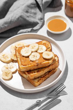 Peçeteli ve gölgeli bir tabakta muzlu fıstık ezmeli tost. Amerikan kahvaltısı için tatlı beslenme ve sağlıklı atıştırmalıklar kavramı. 