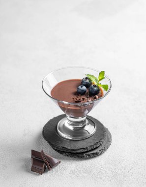 Taze yaban mersinli bardakta çikolatalı puding ve açık arkaplanda çikolata parçalı nane şekeri. Ev yapımı kremalı tatlı ya da panna cotta konsepti. Boşluğu kopyala.