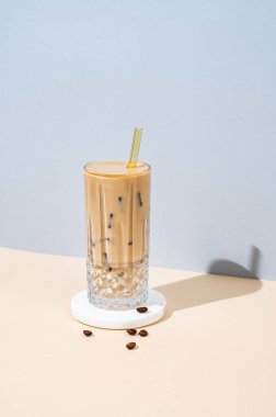 Kahve çekirdekleri ve gölgeli sarı-mavi arka plandaki mermer tezgahta laktozsuz sütsüz, uzun bardakta soğuk latte kahve. Yaz modası konsepti, ferahlatıcı bir vejetaryen içeceği. Boşluğu kopyala.